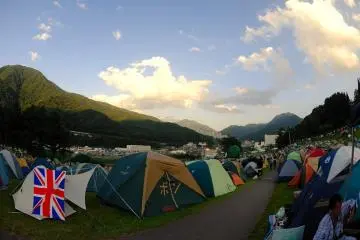 Photo:  Camping at Fuji Rock Festival – <a href="https://en.wikipedia.org/wiki/File:Fujigreenstage.jpg" target="_blank" rel="noreferrer noopener nofollow">Jmills74</a> / <a href="https://creativecommons.org/licenses/by-sa/3.0/deed.en" target="_blank" rel="noreferrer noopener nofollow">CC BY-SA 3.0</a>