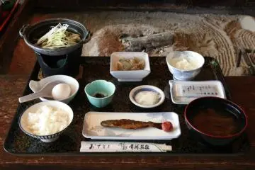Breakfast Menu, starting from the top left - Simmered miso shellfish, stewed butterbur, chinese yam, raw egg (to be poured into the shellfish), kombu, pickled vegetables, flavoured seaweed (nori), rice, sweet boiled rainbow trout, kenojiru (a traditional Tsugaru soup). (Photo: <a href="https://www.aoninet.com/en/index.html" target="_blank" rel="noreferrer noopener nofollow">Aoni Onsen</a> / JT)