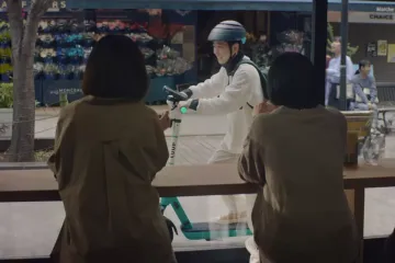 Two people looking out the window of a cafe, seeing someone glide by on a LUUP scooter (Photo: LUUP)